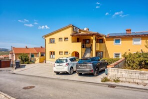 Un edificio giallo di due piani con un tetto in tegole rosse, un portico coperto e una scala che conduce al piano superiore. Due automobili sono parcheggiate nel vialetto.
