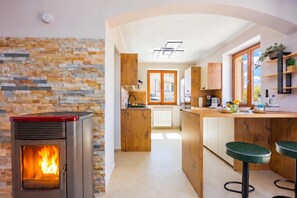 A modern kitchen with a stone wall, a wood-burning stove, and a central island with bar stools. - Double D Modern Family Apartment Near Koper (Koper)