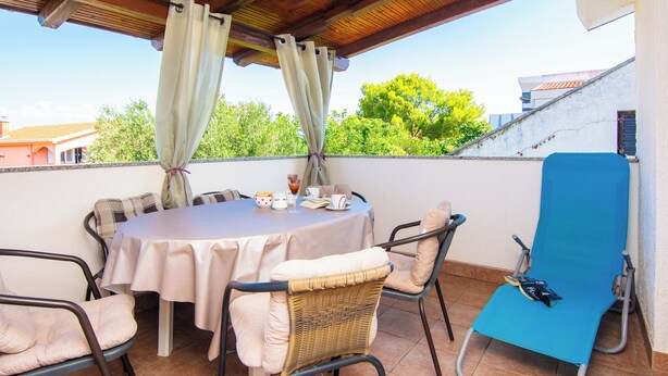 Un patio al aire libre techado con una mesa redonda, cuatro sillas y una butaca azul.