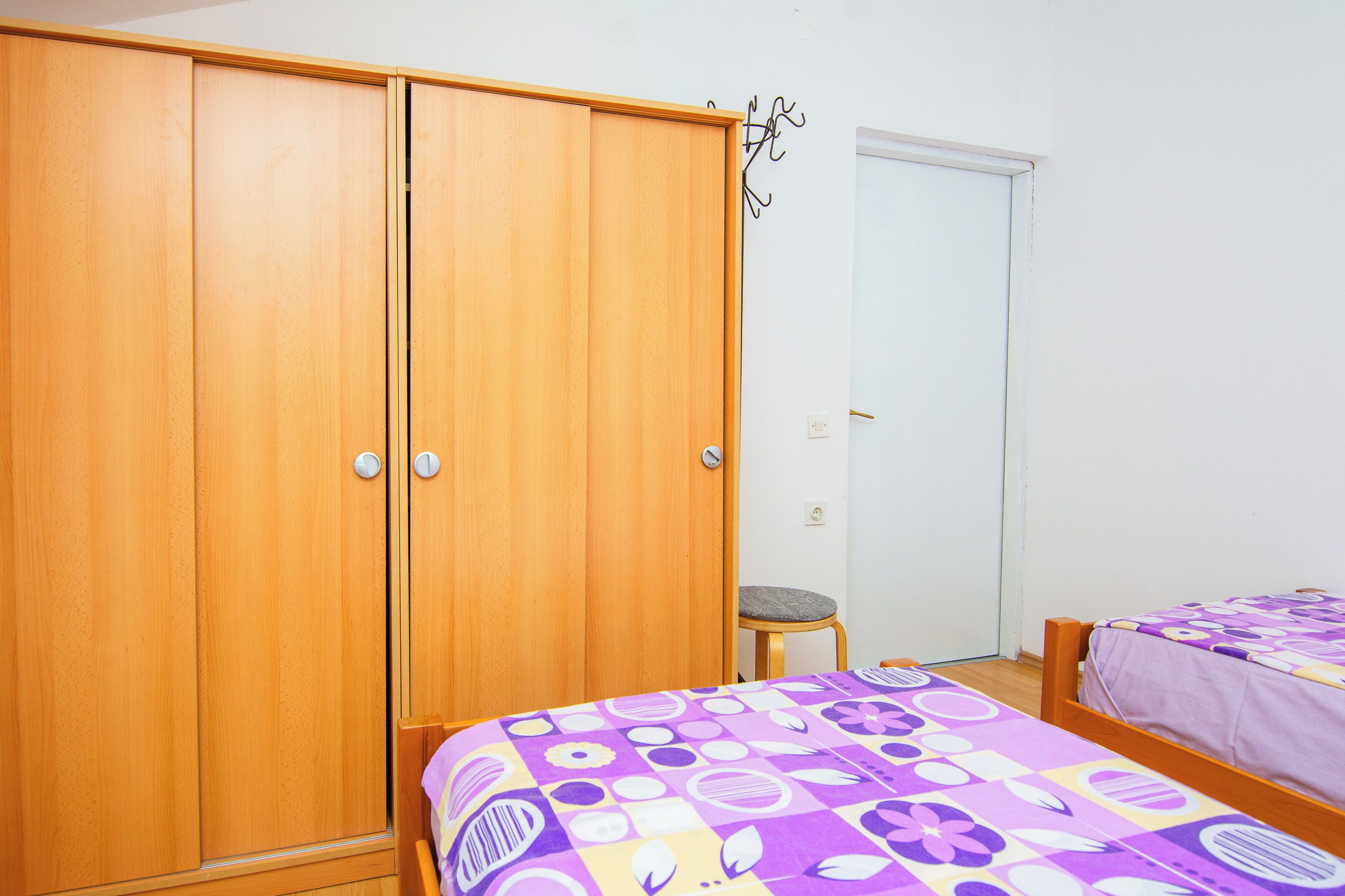 A bedroom with two beds, a wooden wardrobe, and a small stool.