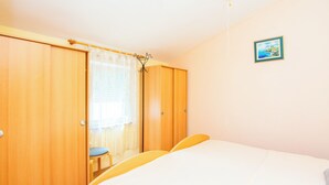 Un dormitorio con una cama, un armario de madera, una silla y un ventanal con cortinas.
