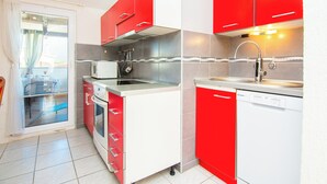 Una cocina compacta con armarios rojos y blancos, horno empotrado, microondas y lavavajillas.