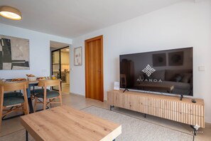 A modern living room with a flat-screen TV, wooden furniture, and a kitchen in the background. - A040 PEÑON DE IFACH 6º A (Calp)