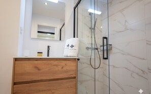 A modern bathroom with a wooden vanity, a glass shower enclosure, and a marble wall.