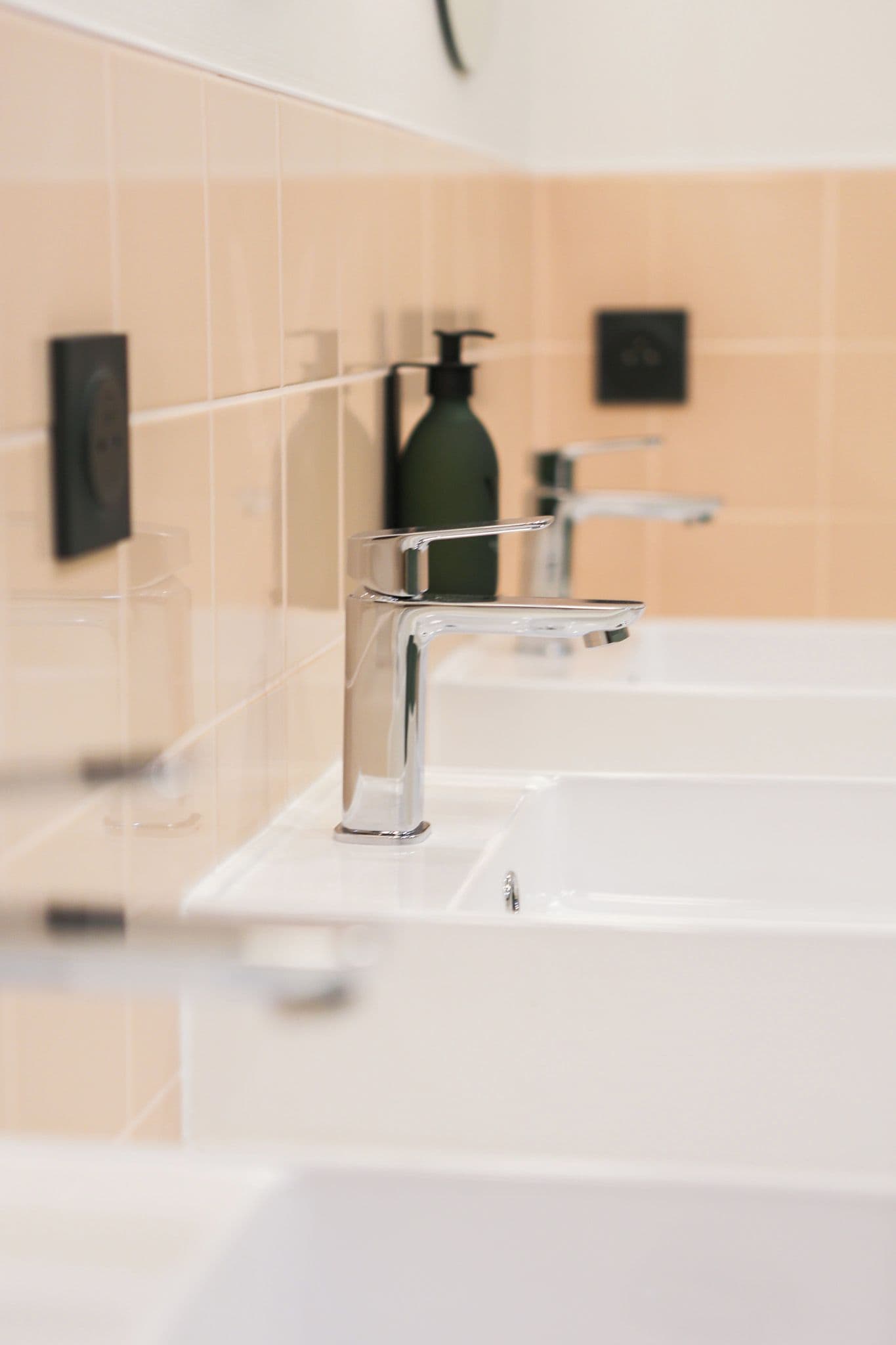 A modern bathroom with a chrome faucet, a glass soap dispenser, and a white sink.