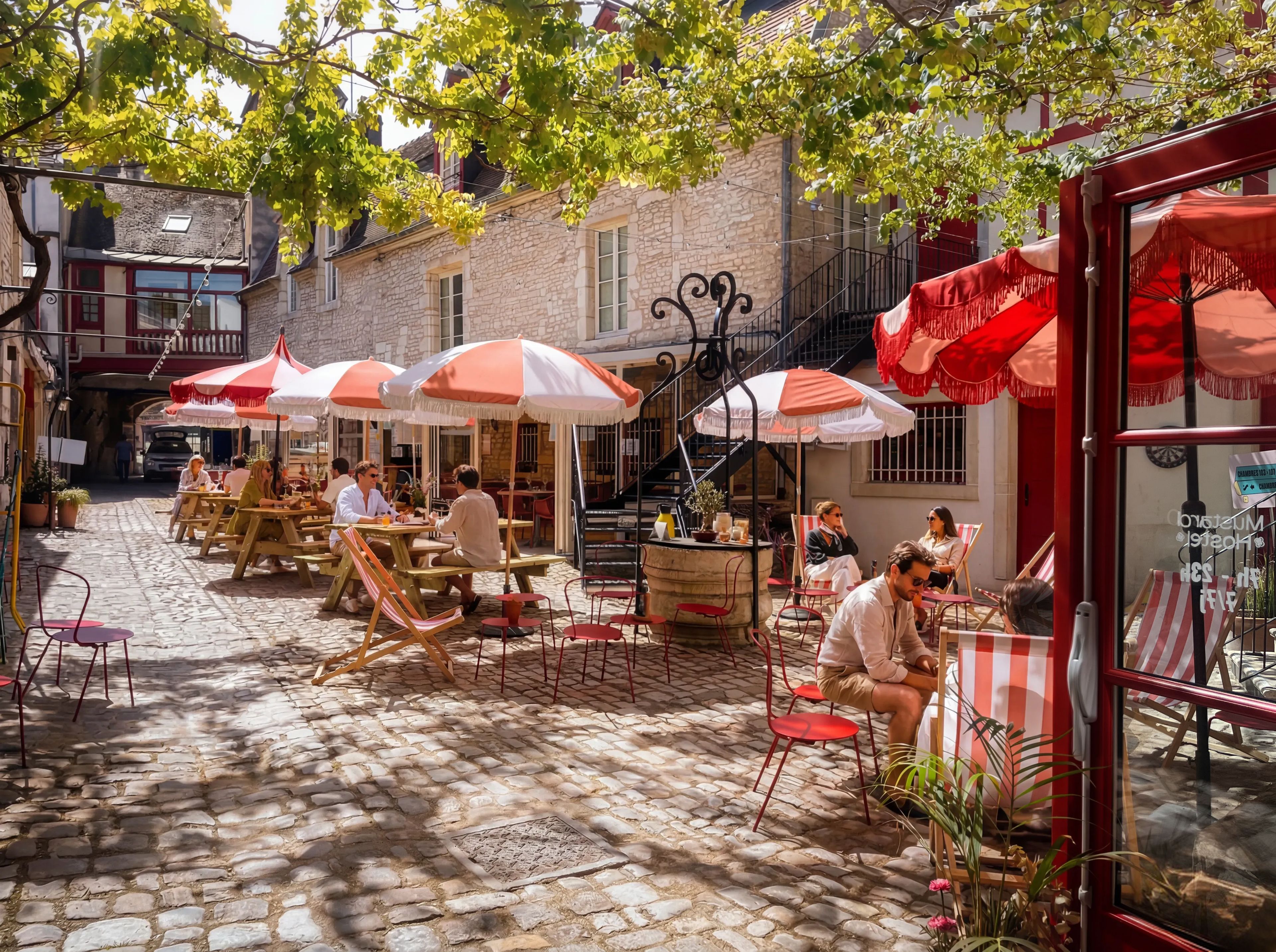Un café en plein air avec un sol en pierre, des parasols à rayures rouges et blanches et des meubles en bois.