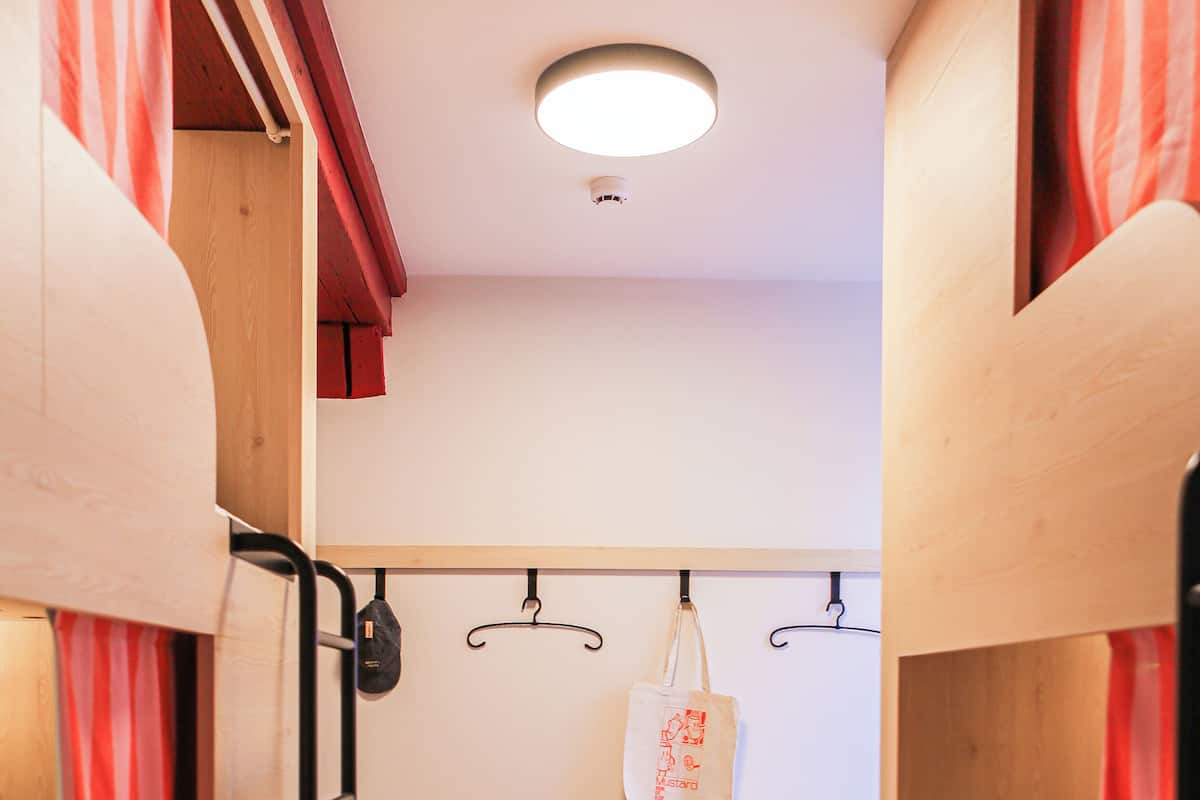 Ein kleines Zimmer mit Etagenbetten, einer kleinen Bank, einer hängenden Tasche und einer Lampe.