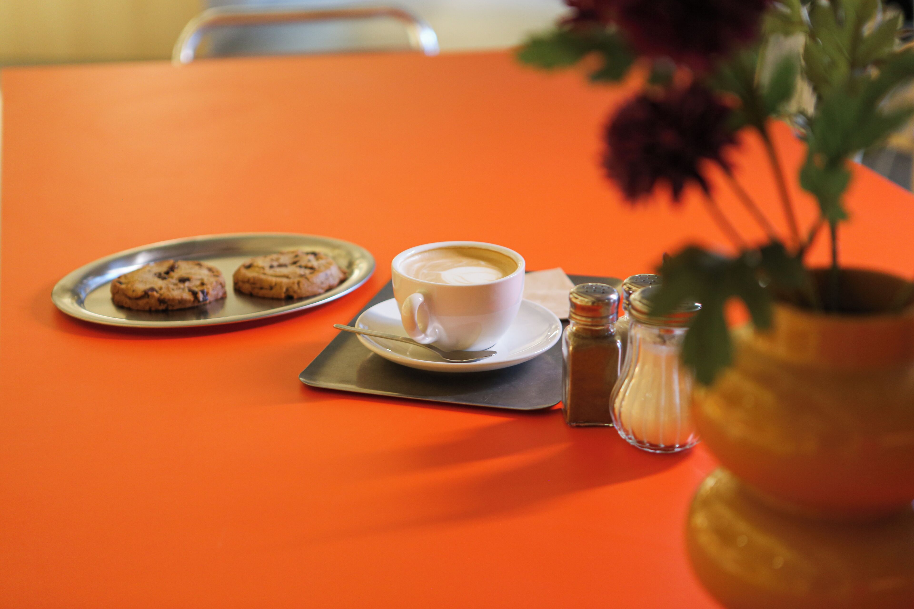 A table with a cup of coffee, a plate of cookies, and a salt shaker.