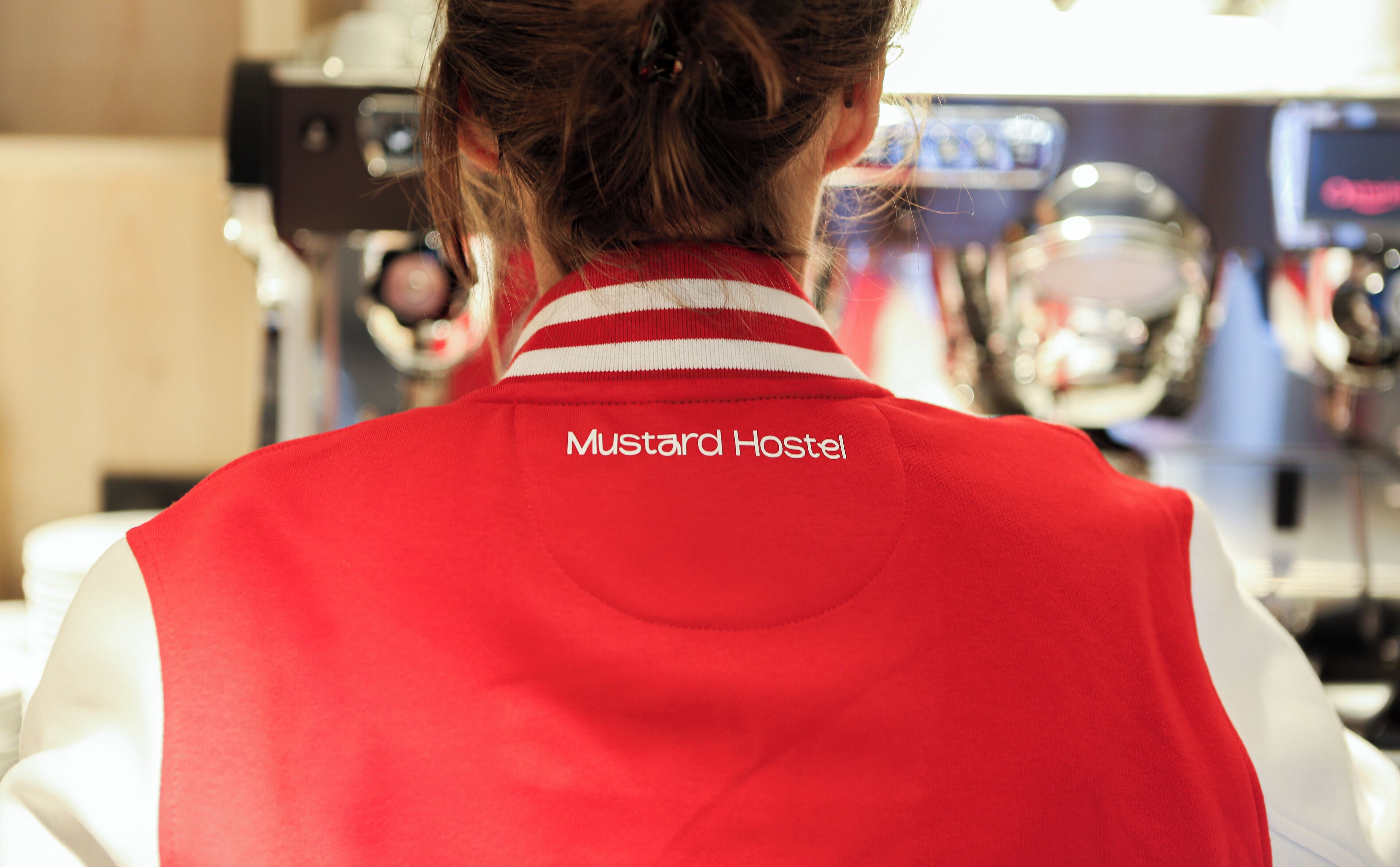 Une personne portant un gilet rouge sur lequel est écrit « Mustard Hostel ».