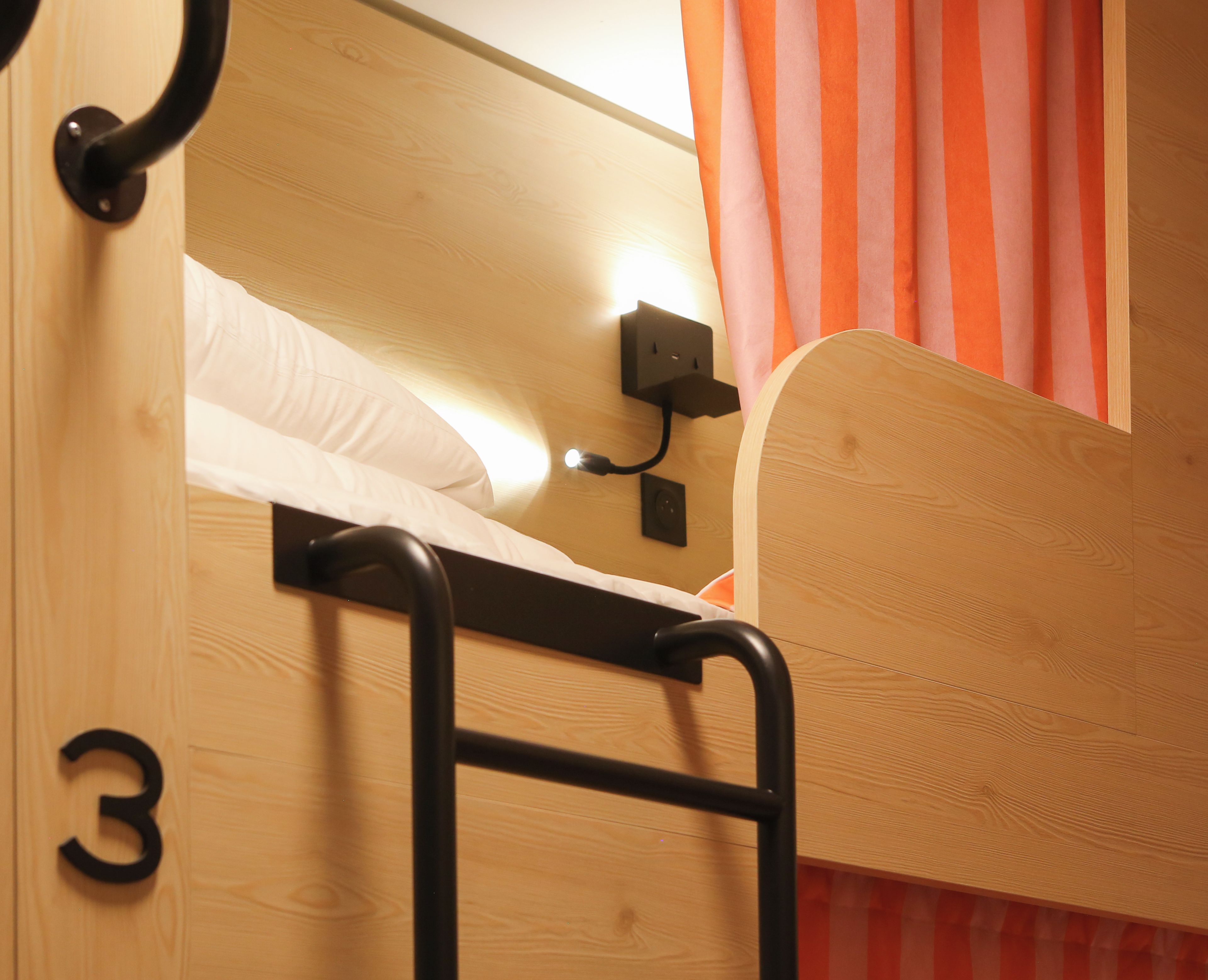 Ein Stockbett mit einer Leiter, eine an der Wand befestigte Steckdose und die Zahl '3' auf der Tür.