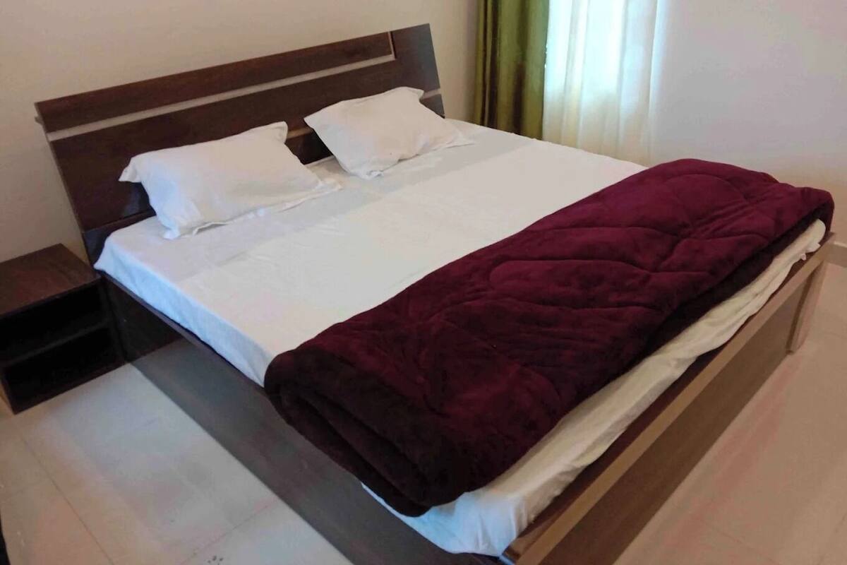 Una cama con cabecera de madera, ropa de cama blanca y una manta rojo oscuro.