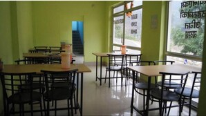 A room with tables and chairs, a staircase, and a window with text. - Hotel Dev Darshan & Restaurant (Bhatwari)
