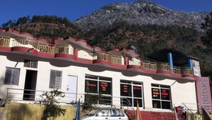 A hotel with a balcony, multiple windows, and a mountainous backdrop. - Hotel Dev Darshan & Restaurant (Bhatwari)