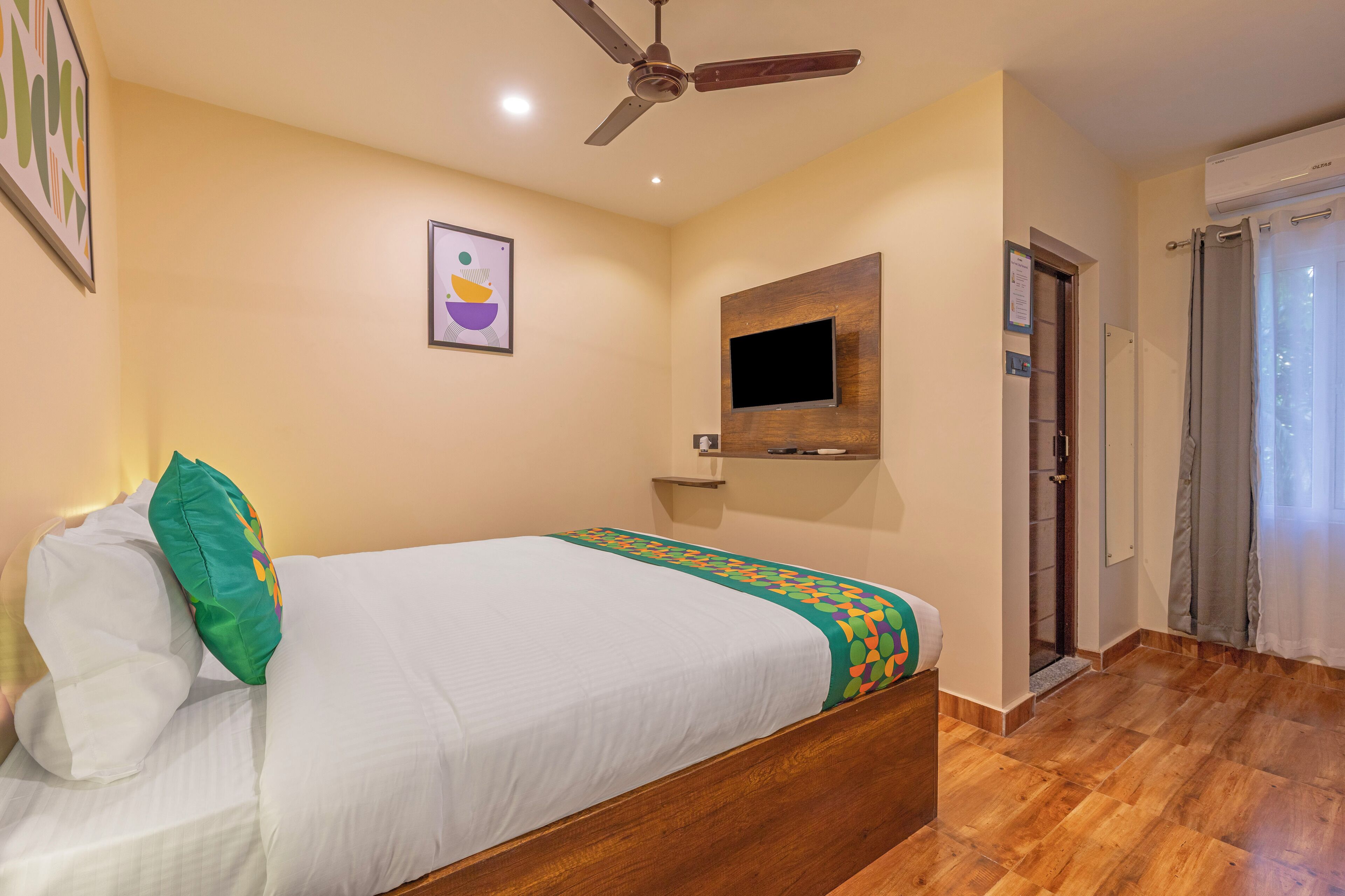Une chambre d’hôtel avec un lit, un ventilateur de plafond, un téléviseur fixé au mur, une porte et une fenêtre.