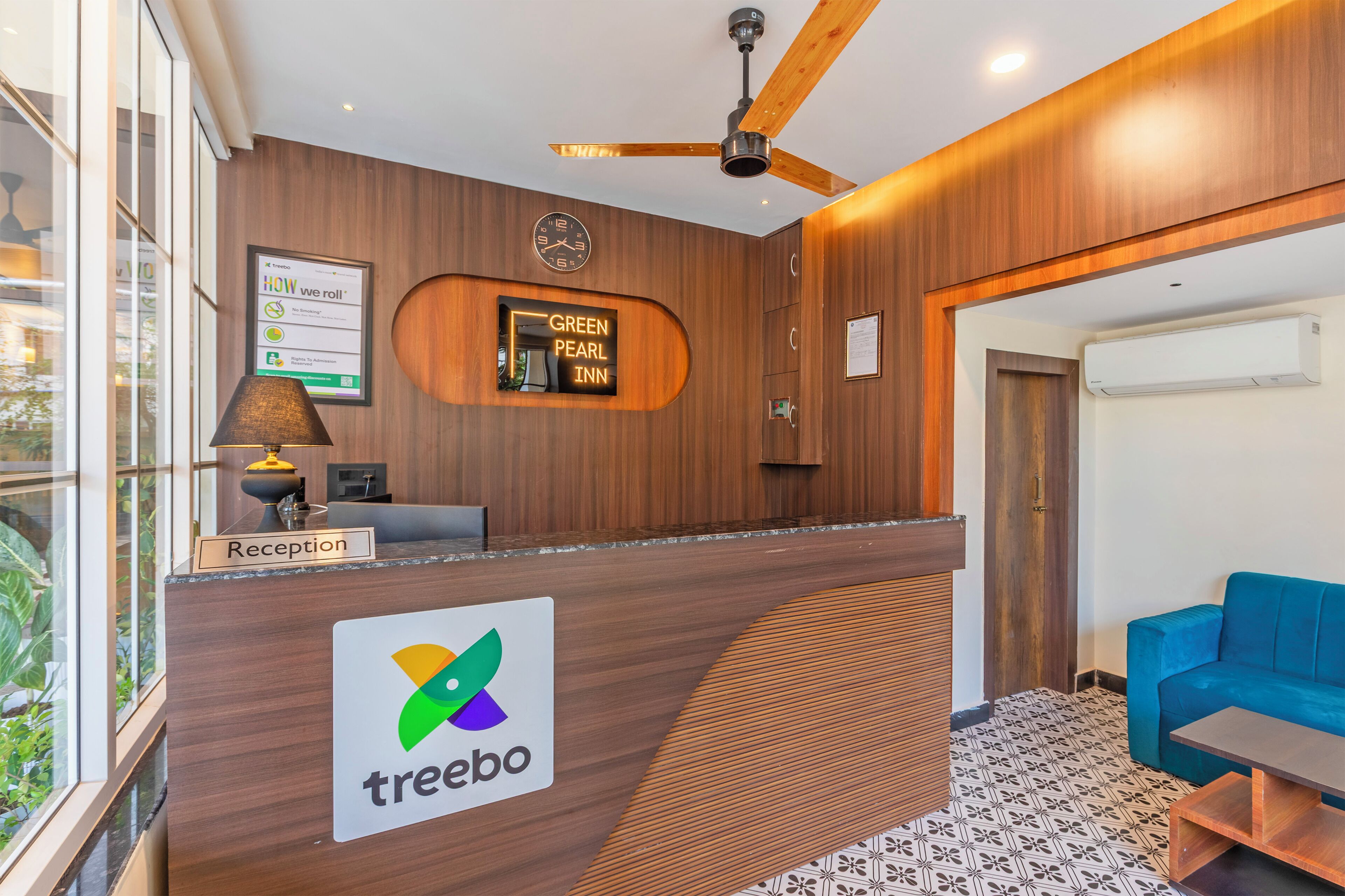 En receptionsdisk med en logo, et ur og et skilt med 'Green Pearl Inn'.