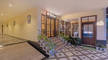 A hotel lobby with a staircase, potted plants, a reception desk, and a sign for a restaurant.