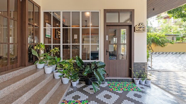 Entrada de hotel com balcão de recepção, plantas em vasos e área de acesso revestida em azulejos.