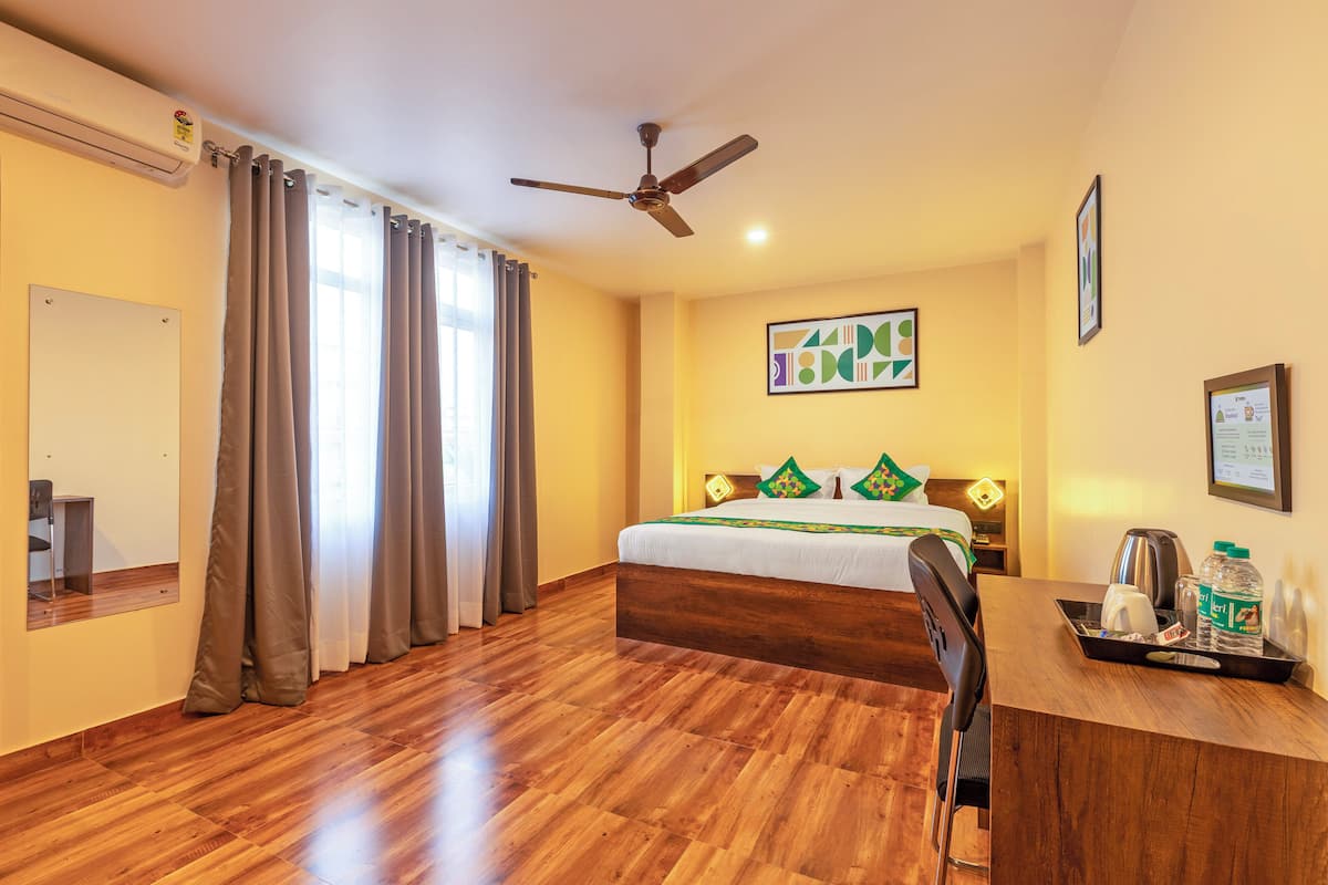 A hotel room with a bed, a desk, a chair, a ceiling fan, and a window with curtains.