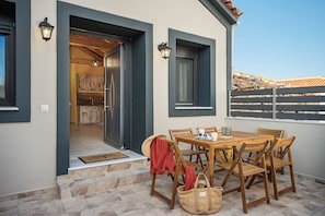 A wooden table with chairs and a basket outside a building with a door leading to an interior space. - Sirius House (Mitilinii)