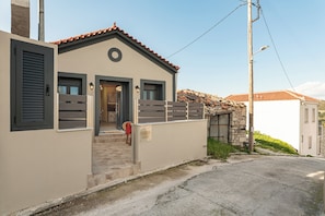 A two-story building with a beige facade, a red-tiled roof, and a stone wall. - Sirius House (Mitilinii)