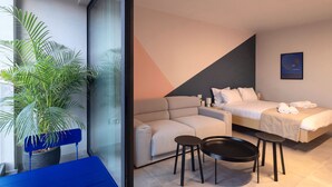 Ein modernes Hotelzimmer mit einer Couch, einem Bett, einem kleinen Tisch und einer Topfpflanze.