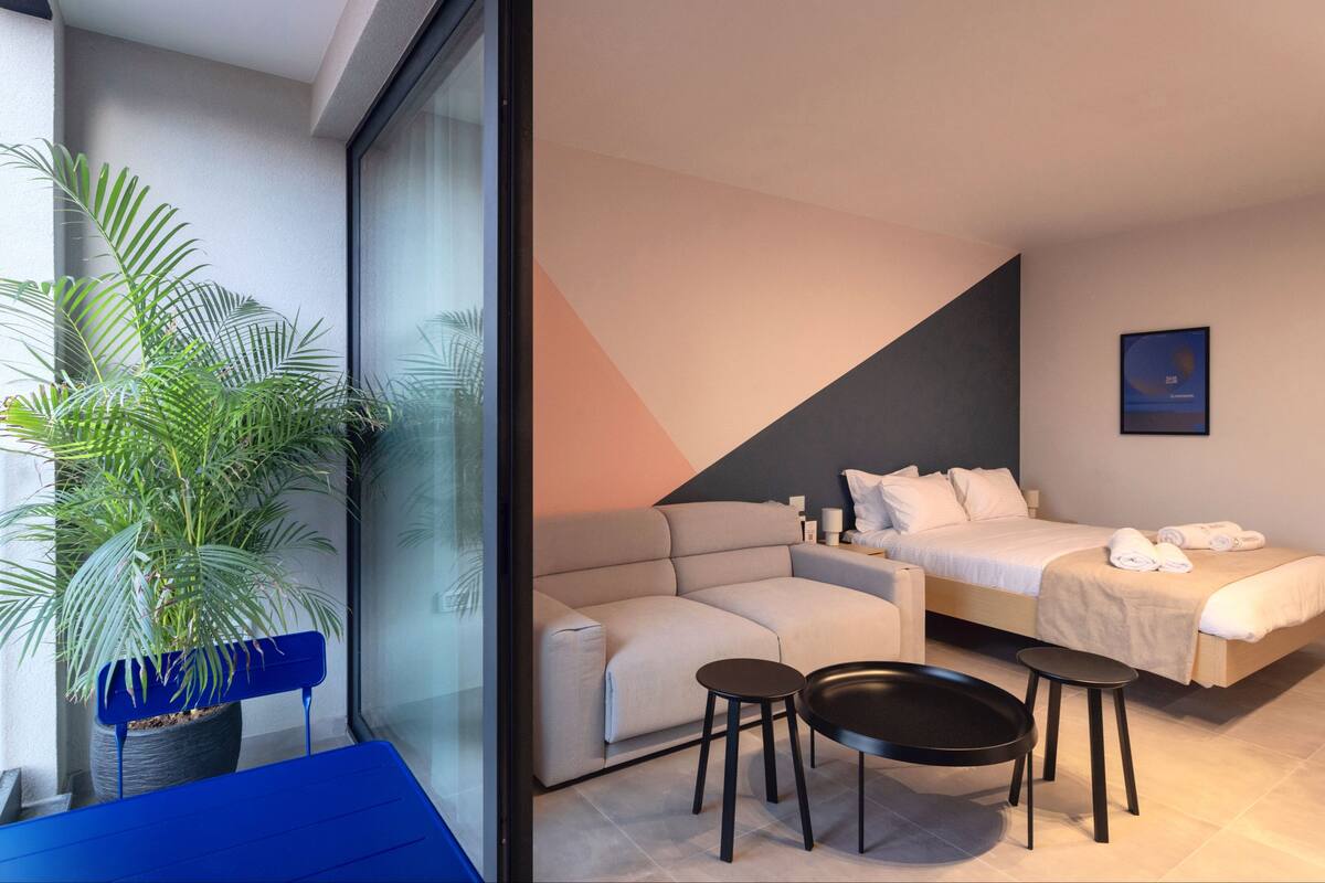 A modern hotel room with a sofa, a bed, a small table, and a potted plant.