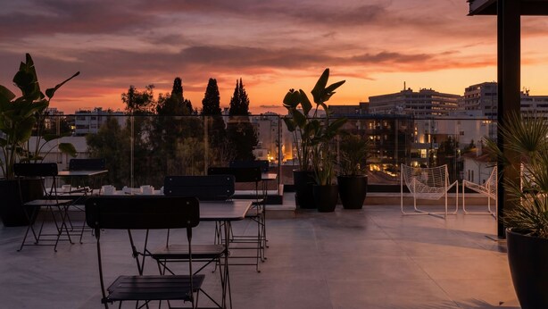 Eine Terrassensitzgelegenheit mit Töpfen und Pflanzen mit Blick auf eine Stadtlandschaft bei Sonnenuntergang.
