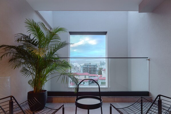 Un balcón con planta en maceta, una silla y vistas a edificios a través de un ventanal grande.