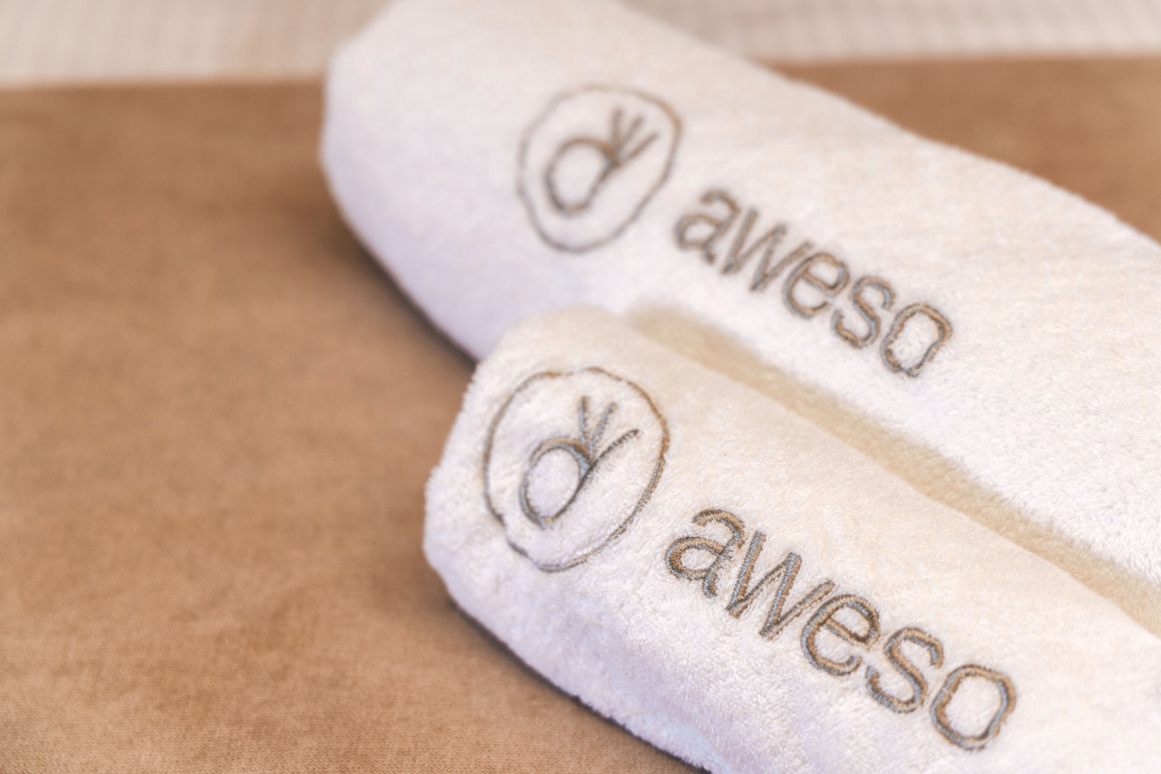 Two white towels with embroidered text and a logo.
