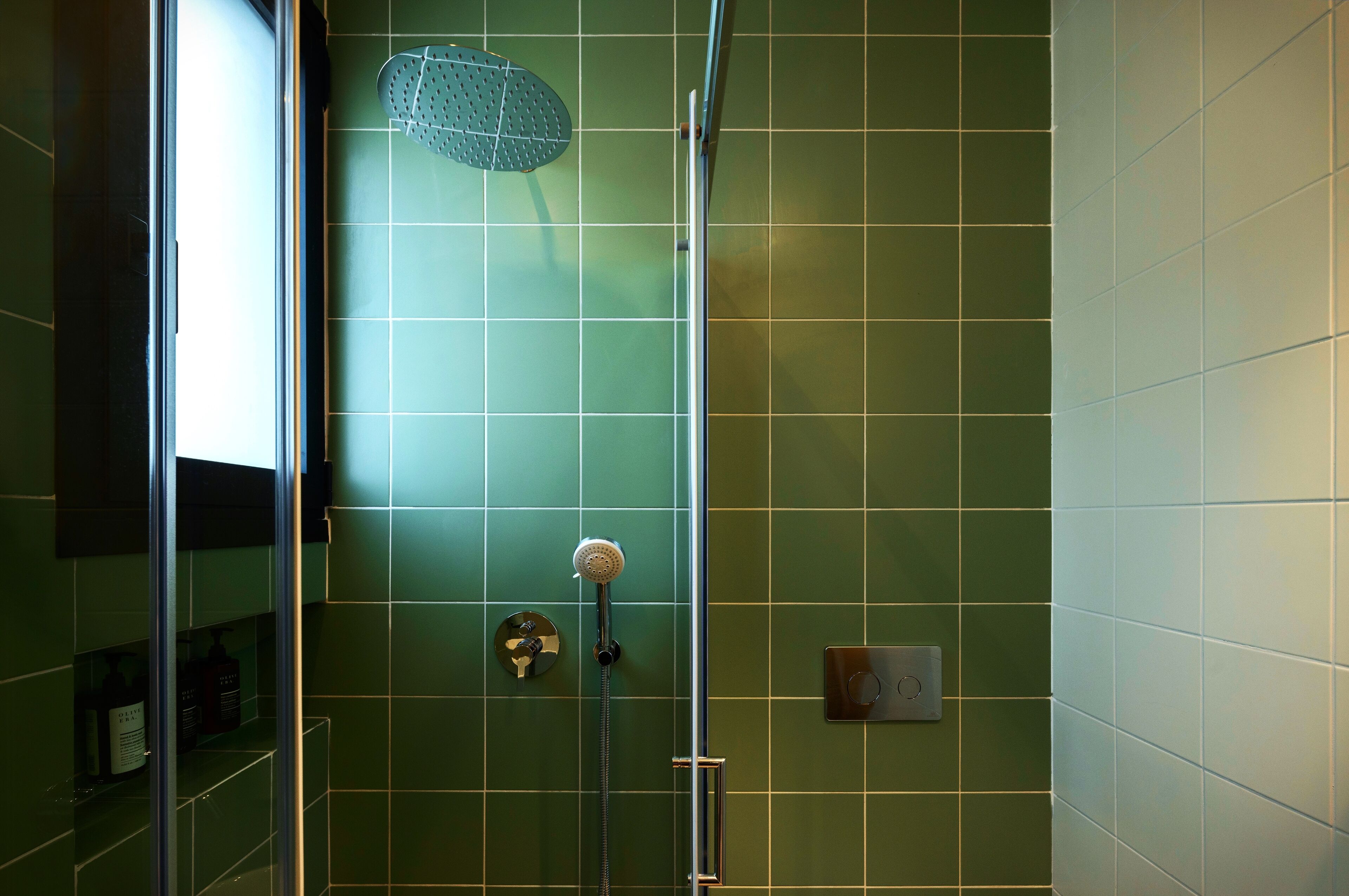 Un baño con azulejos verdes, una ducha con cabezal de ducha de mano y una puerta de vidrio.