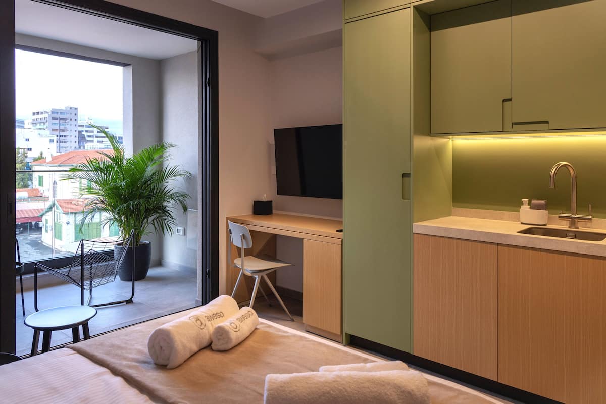 A modern hotel room with a balcony, a desk, a chair, a TV, and a sink.