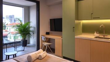 Una habitación de hotel moderna con balcón, un escritorio, una silla, un televisor y un lavamanos.