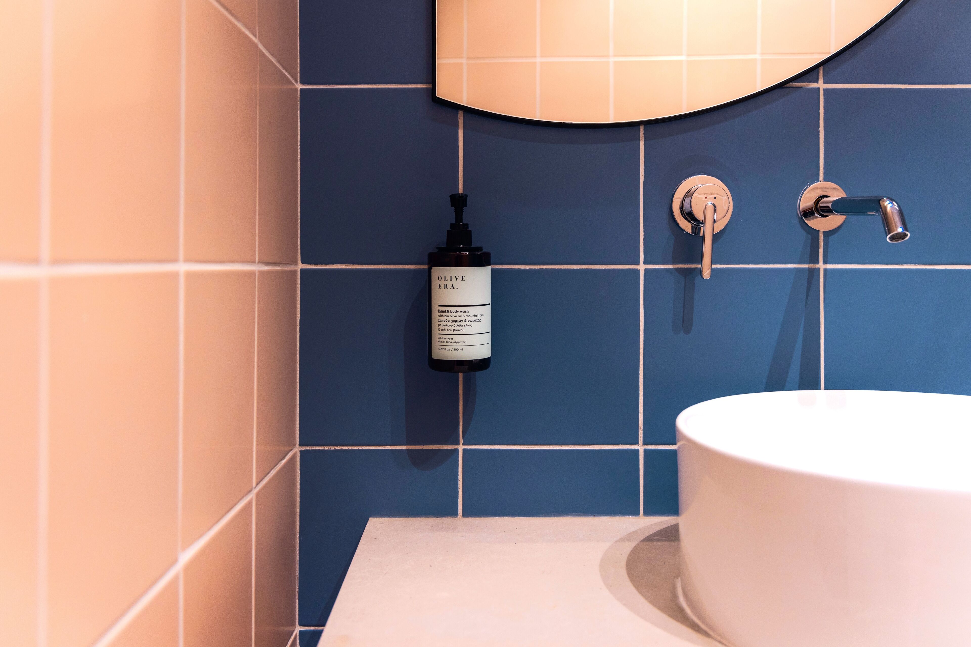 A bathroom with blue tiles, a white sink, and a bottle of olive oil.