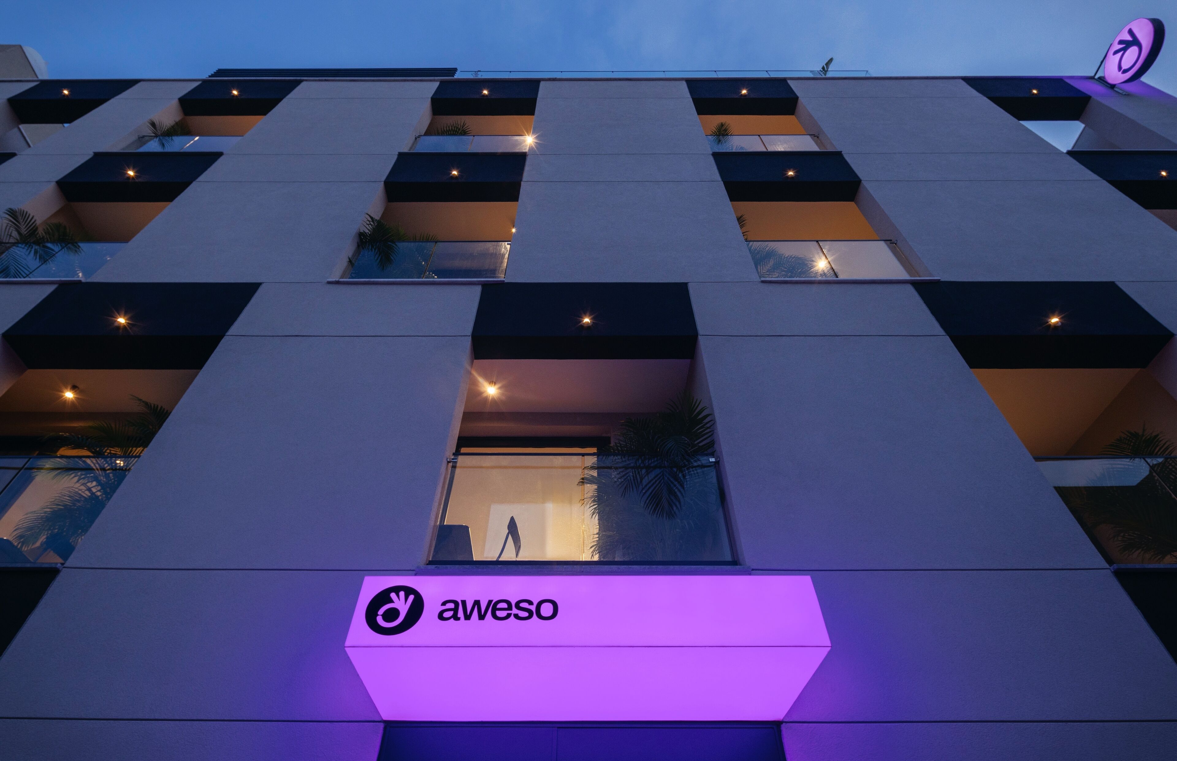 A modern building with a prominent aweso logo, multiple balconies, and a well-lit entrance.