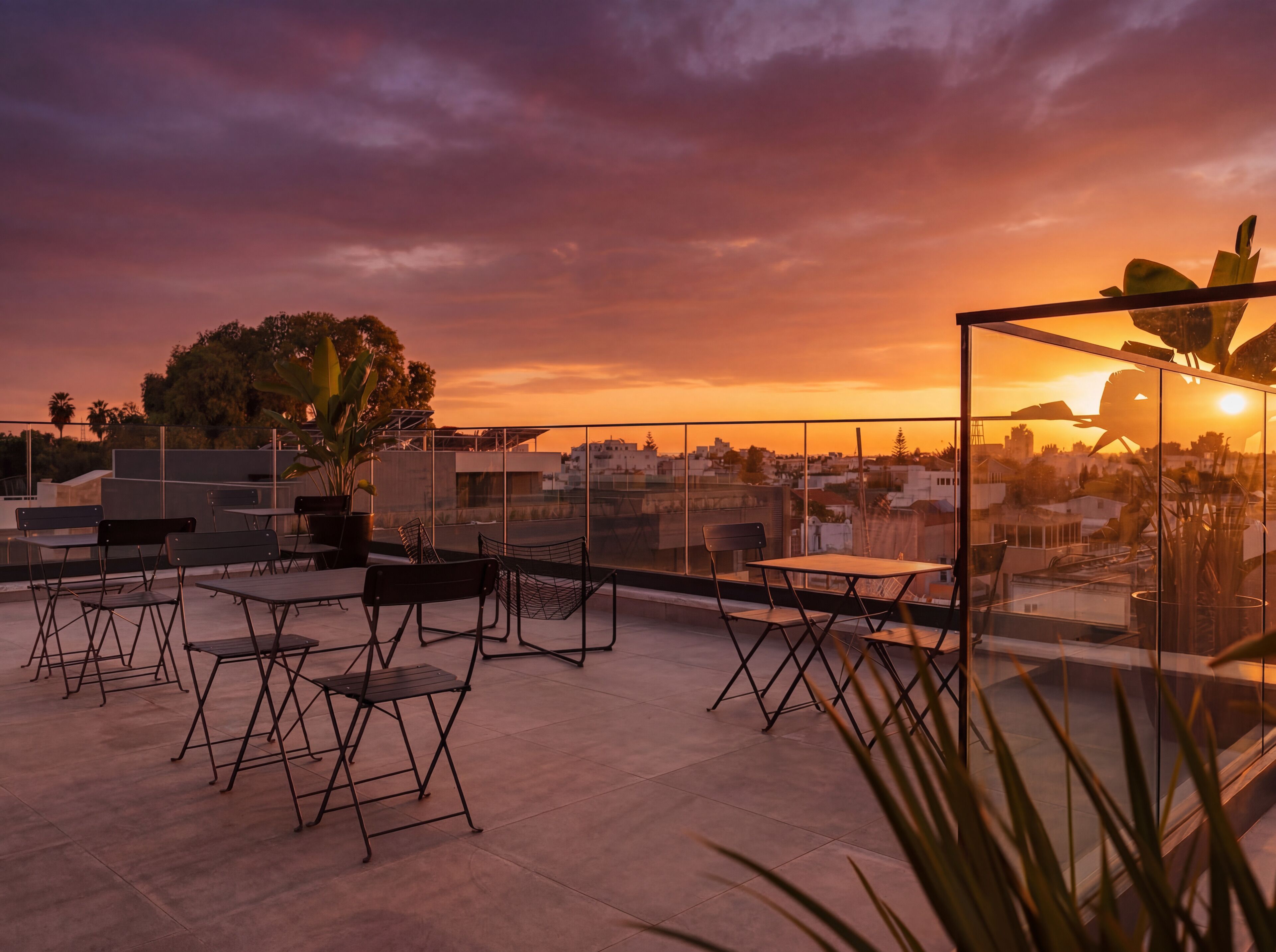 Un espace extérieur aménagé avec des tables et des chaises, offrant une vue sur le paysage urbain au coucher du soleil.
