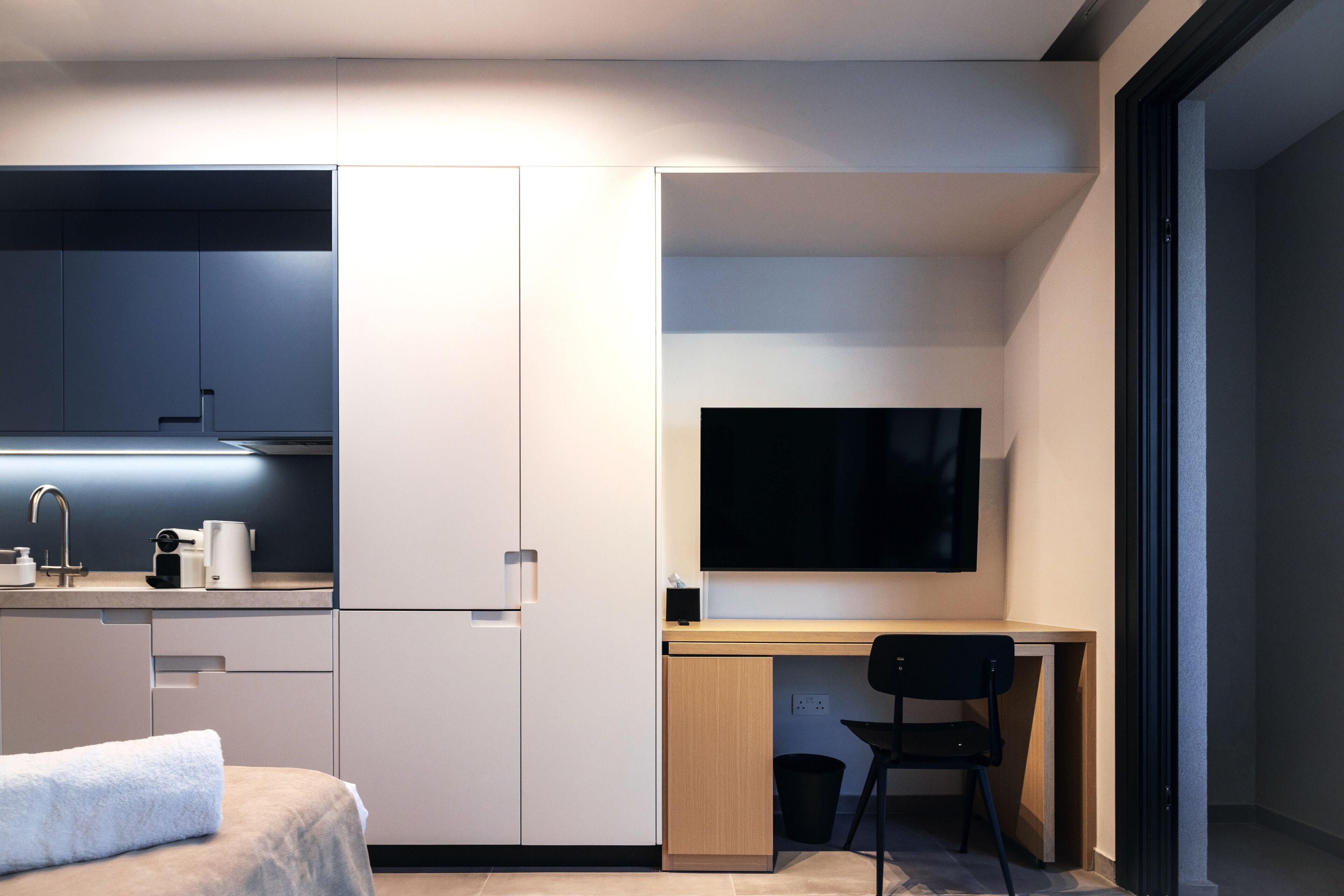 Una habitación compacta y moderna, con kitchenette, una cama, un escritorio con silla y un televisor de pantalla plana.