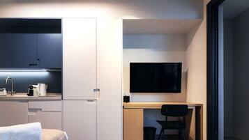 Una habitación compacta y moderna, con kitchenette, una cama, un escritorio con silla y un televisor de pantalla plana.