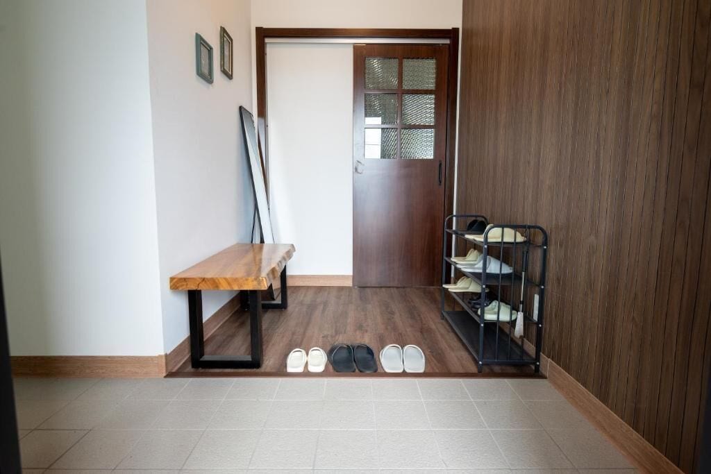 Ein Flur mit einer hölzernen Bank, einem Schuhregal mit Schuhen und einer Tür mit Milchglasfüllung.