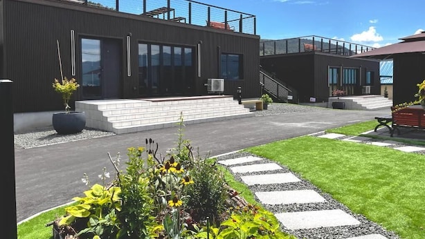 A modern building with a flat roof, large windows, and a covered outdoor area with steps leading to a door. - Furano Torinuma VILLA (Furano)