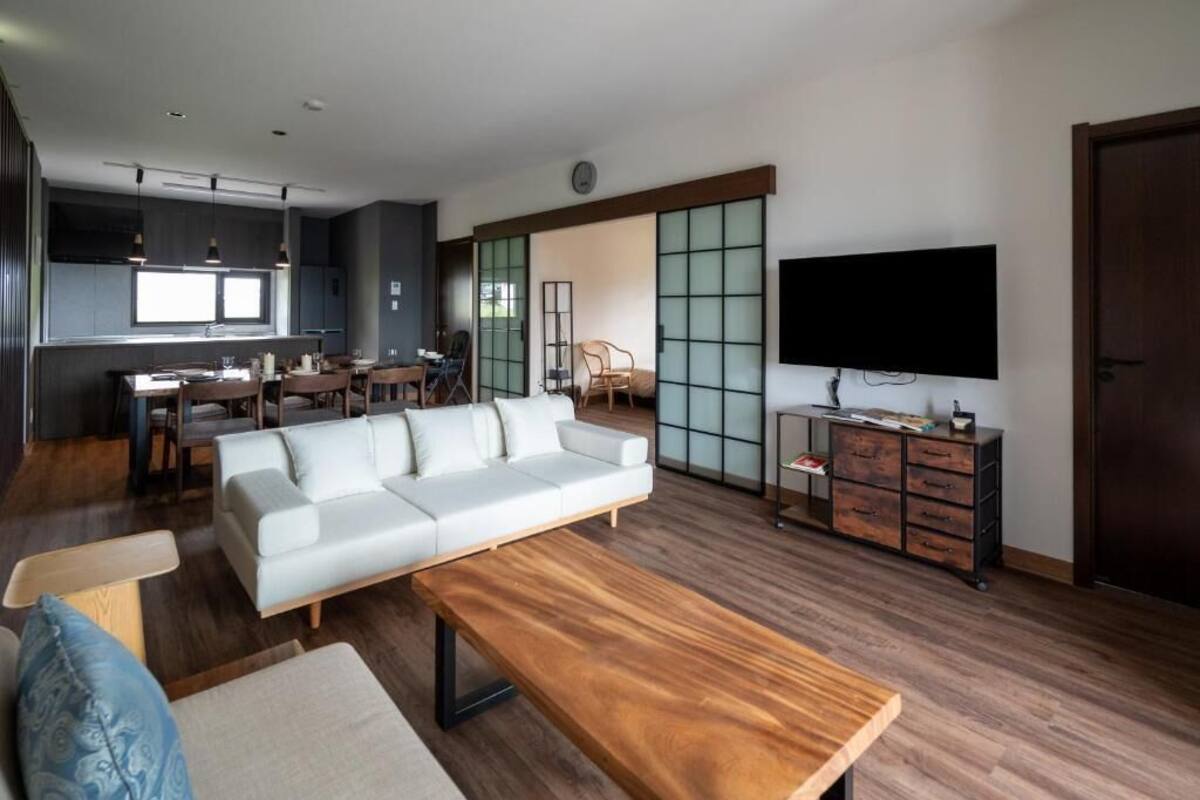 Een moderne woonkamer met een bank, salontafel en televisie. Er is een eethoek met stoelen en een tafel.