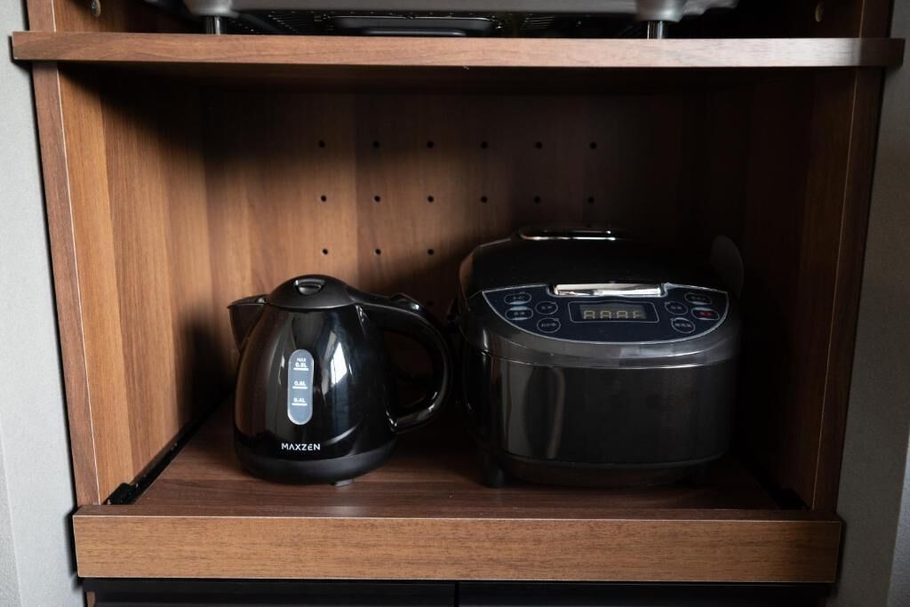 A wooden shelf with a black electric kettle and a rice cooker.