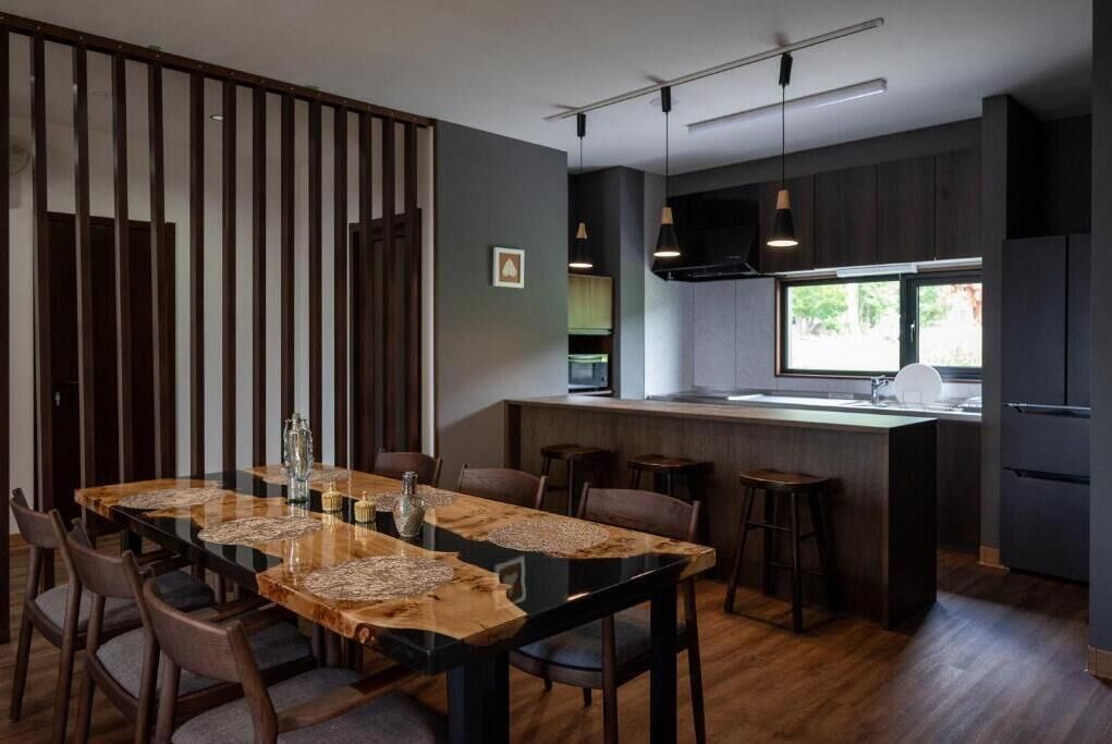 Een moderne keuken met een centraal eiland, donkere keukenkastjes, en een eethoek met een houten tafel en stoelen.