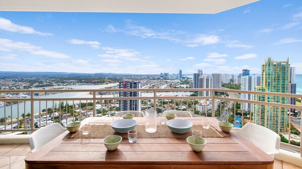 A balcony with a table set for dining, overlooking a cityscape with high-rise buildings and a river.
