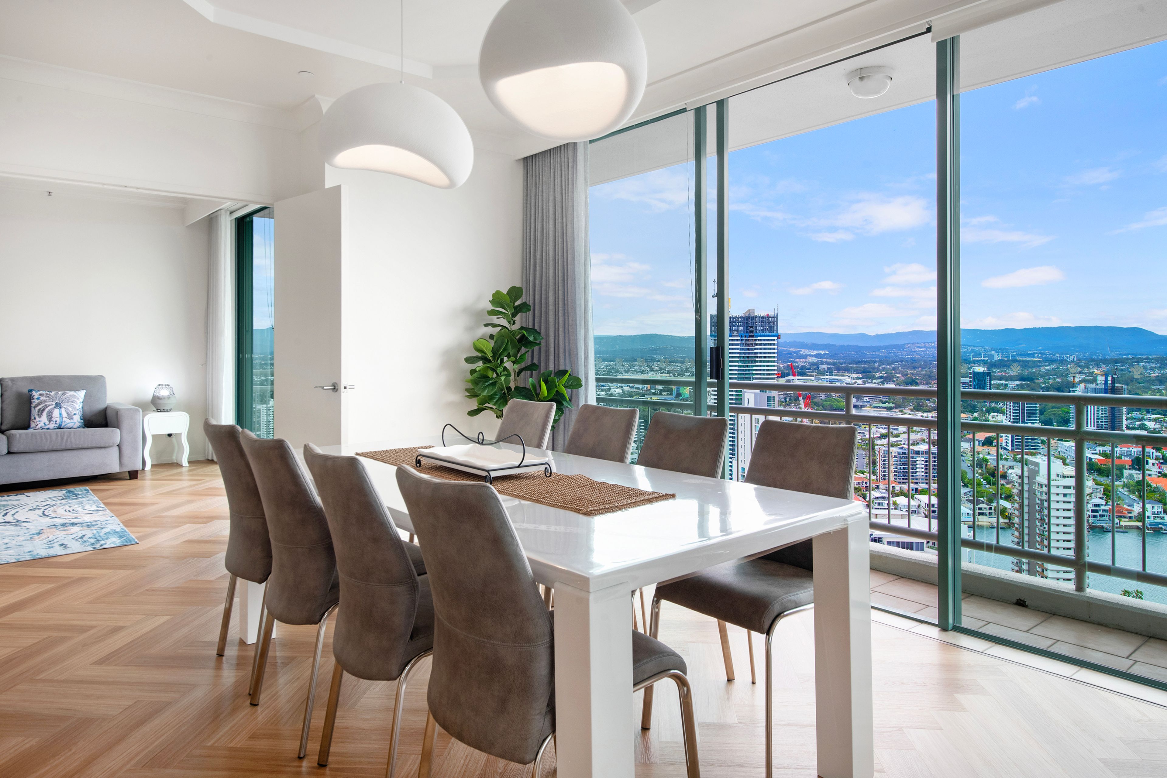 Een moderne eethoek met een witte tafel, grijze stoelen en uitzicht op een stadsgezicht door grote ramen.