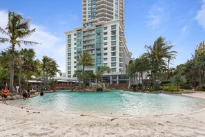 A resort with a swimming pool, palm trees, and a tall building in the background. - Crown On Palm Surfers Paradise with Resort Access (Surfers Paradise)