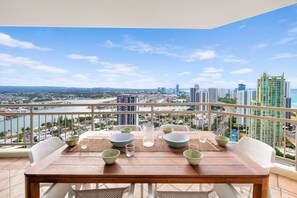 En balkon med et træbord dækket til spisning, med udsigt over et bybillede med bygninger og en flod.