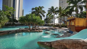 A pool area with clear water, palm trees, and a wooden boat structure.