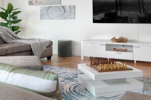 A modern living room with a sofa, a coffee table with chess pieces, a television, and a plant.