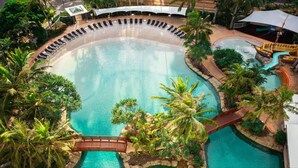 Ein großer, gewölbter Swimmingpool mit einer Holzbrücke und Palmen.