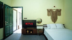 Een kamer met een bed, een televisie waarop 'NETFLIX' staat, een klein tafeltje en een decoratie aan de muur.